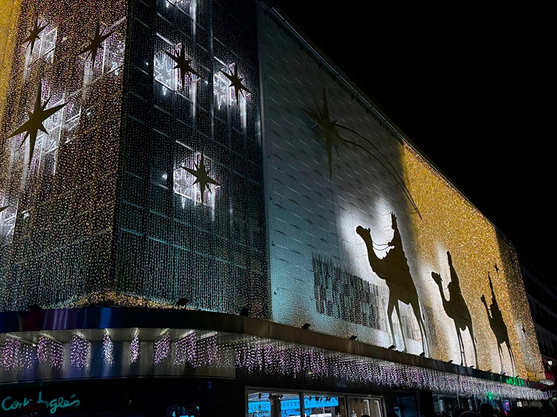 Рождественская иллюминация на фасаде El Corte Ingl&eacute;s в районе Preciados&ndash;Callao в Мадриде, золотые огни и силуэты Трех королей на верблюдах на ночном небе