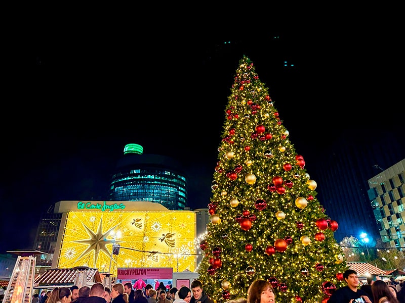 Большая рождественская ёлка на Mercado de Navidad у El Corte Ingl&eacute;s Castellana в Мадриде, на заднем плане световой фасад с золотой звездой и ангелами