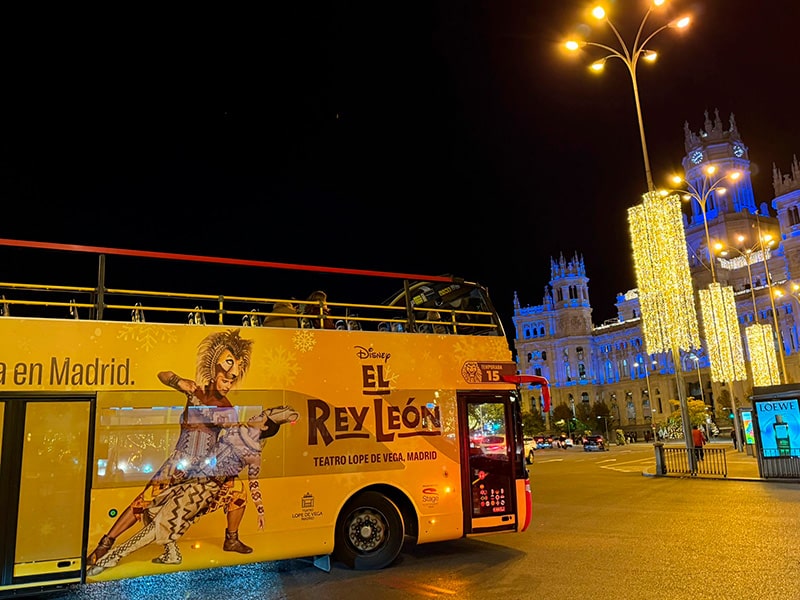 Туристический двухэтажный автобус с рекламой мюзикла El Rey Le&oacute;n на Plaza de Cibeles в Мадриде, на заднем плане подсвеченный Palacio de Cibeles и рождественская иллюминация  Название файла (транслит, без пробелов):